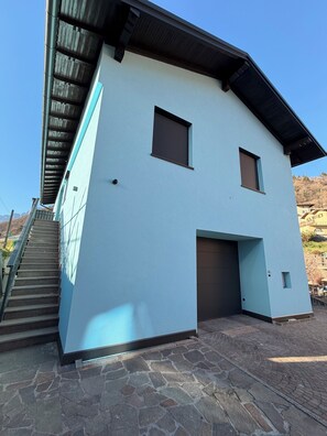 Ein zweistöckiges Gebäude mit hellblau gestrichener Fassade, einer überdachten Treppe und einem Garageneingang.