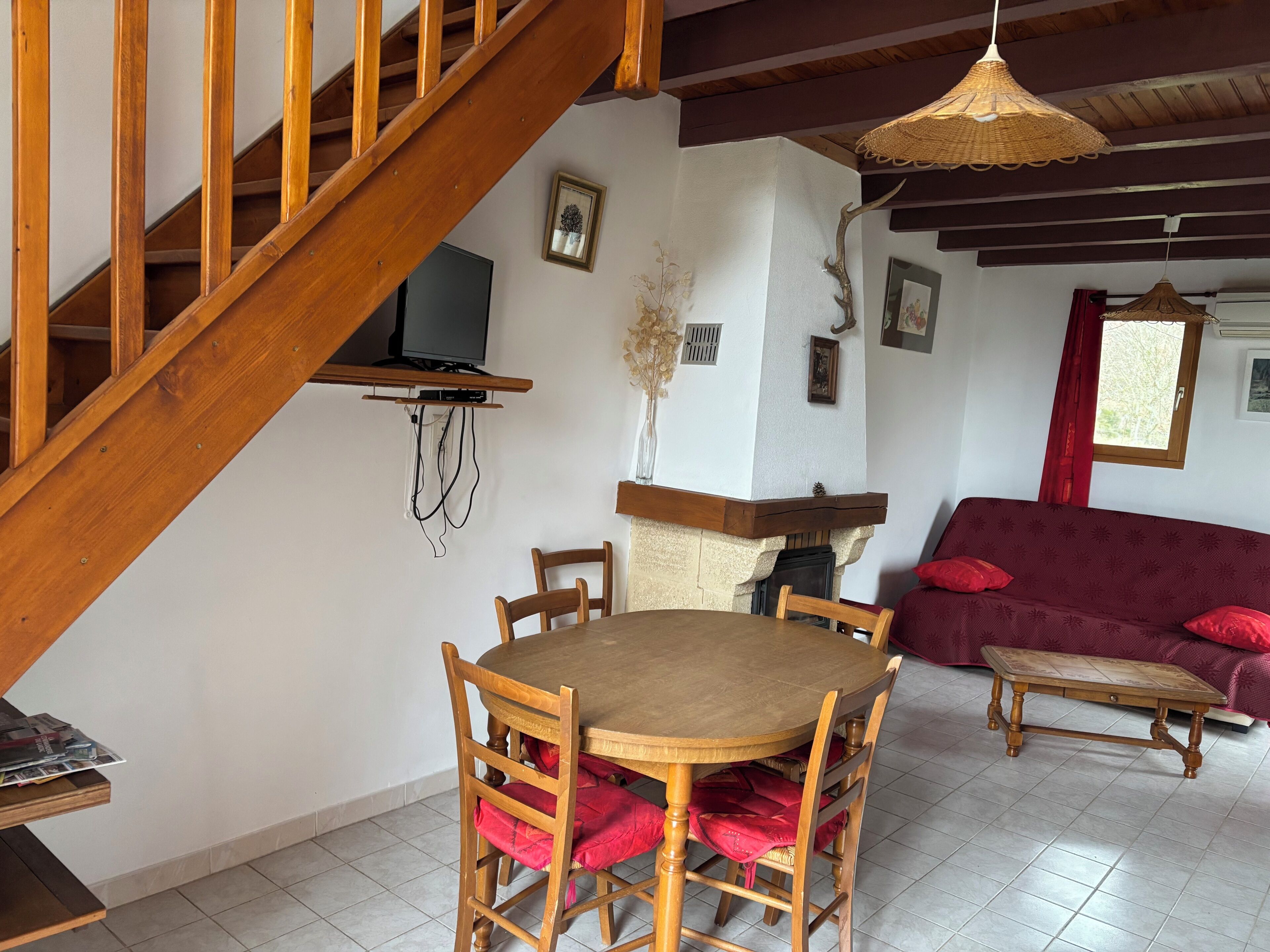 Un escalier en bois, une table à manger avec des chaises, un canapé et un téléviseur fixé au mur.