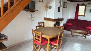 Un escalier en bois, une table à manger avec des chaises, un canapé et un téléviseur fixé au mur.