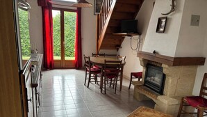 Un coin repas avec une table et des chaises en bois, une cheminée et un téléviseur fixé à une poutre en bois.
