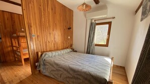 Une chambre avec un plancher en bois, un lit recouvert d’une couvre-lit à motifs, une fenêtre avec des rideaux et un luminaire suspendu.