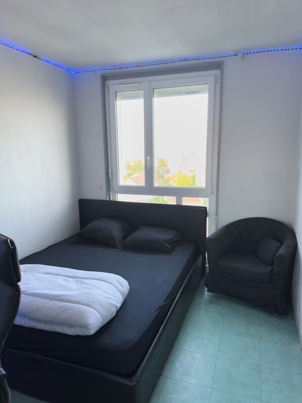 Une chambre Ă coucher avec un lit, une chaise, une fenĂȘtre et des lumiĂšres LED bleues le long du plafond.