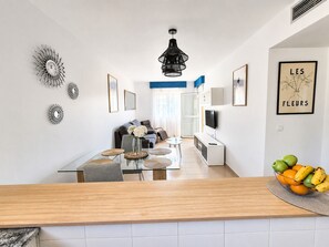 A modern kitchen with a wooden countertop, a dining area with a glass table, and a living space with a sofa and TV.