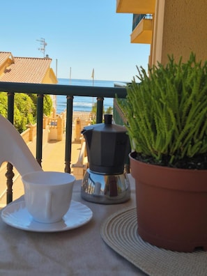 A balcony with a view of the sea, a coffee maker, a cup, and a potted plant.