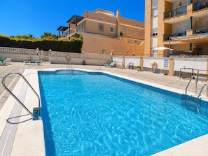 A swimming pool with a clear blue water, surrounded by a tiled deck and a low wall.