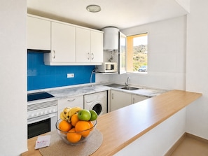A modern kitchen with white cabinets, a blue backsplash, a microwave, a sink, and a fruit bowl on the counter.