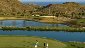 Un campo de golf con un estanque, búnkeres de arena y vistas claras de las colinas circundantes.