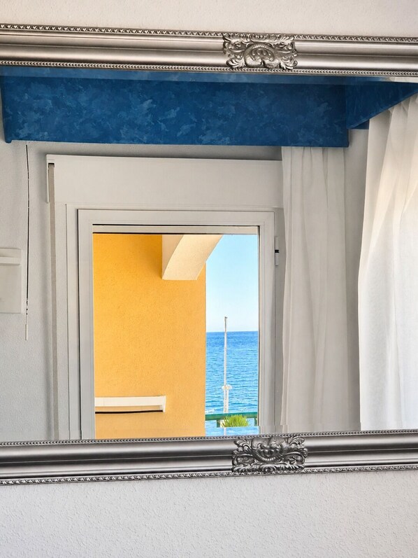 A room with a door leading to a balcony with a view of the sea.