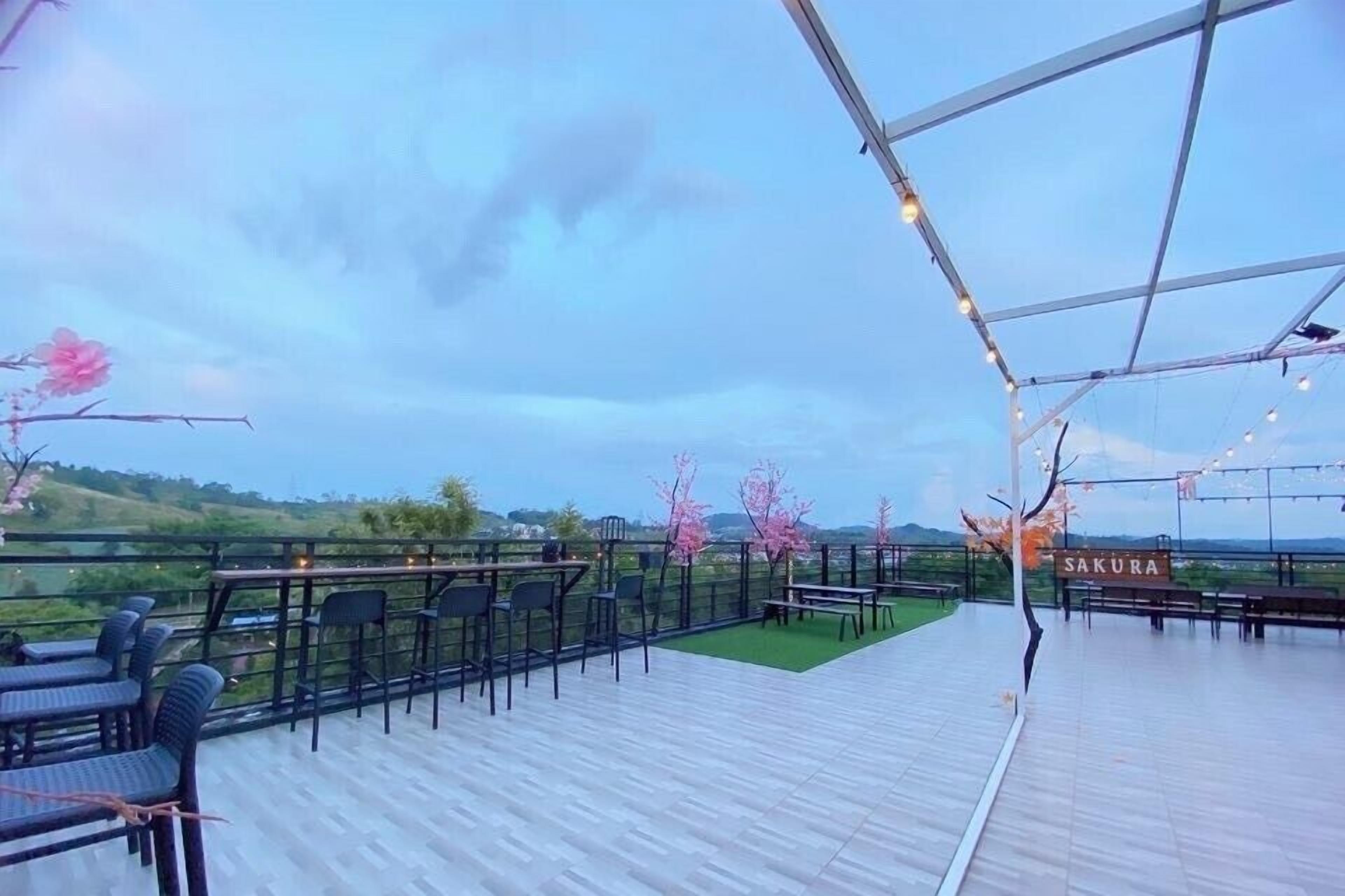 An outdoor terrace with tables and chairs, a sign reading 'SAKURA', and a view of the landscape.