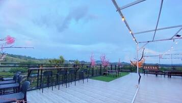 An outdoor terrace with tables and chairs, a sign reading 'SAKURA', and a view of the landscape.
