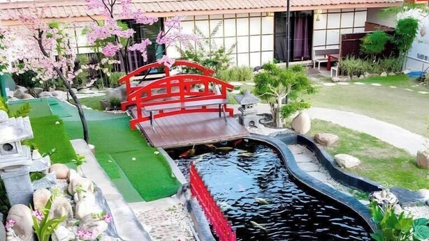 A koi pond with a red bridge, surrounded by rocks and plants. - Sakura Yama Resort (Khaem Son)
