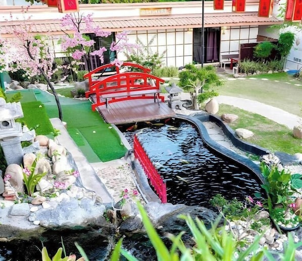Un estanque de carpas con un puente rojo, rodeado de rocas y plantas.