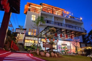 A multi-story hotel with a covered entrance, signage in a foreign language, and a well-maintained garden area.