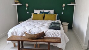 A bed with white bedding, a wooden bench, a woven basket, and a green wall with two white shelves. - Charming winegrower's farmhouse/villa recently renovated with swimming pool max 14 pers. (Marsillargues)