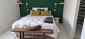 A bed with white bedding, a wooden bench, a woven basket, and a green wall with two white shelves. - Charming winegrower's farmhouse/villa recently renovated with swimming pool max 14 pers. (Marsillargues)