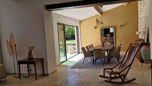 A dining area with a large table, chairs, a rocking chair, and a view through a glass door to an outdoor space. - Charming winegrower's farmhouse/villa recently renovated with swimming pool max 14 pers. (Marsillargues)