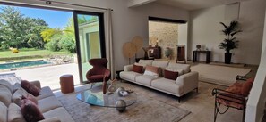 A modern living room with a glass coffee table, a sofa, and a red chair. There is a pool visible through the glass door.