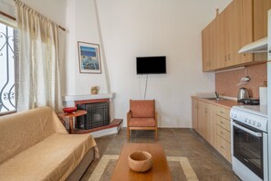 Ein Wohnzimmer mit einer Couch, einem Sessel, einem Kamin, einem Fernseher und einer Küchenzeile mit Schränken und einem Herd.
