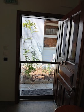An interior doorway leading to an outdoor area with a small garden, a wooden door, and a metal grate at the entrance. - Villa Anty Holiday Home in Sani, Chalkidiki—Private Terrace & Pine Forest Views (Sane)