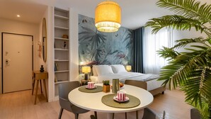 Camera d'albergo con un letto, abat-jour, un tavolo da pranzo con tovagliette, una libreria e una pianta di grandi dimensioni.