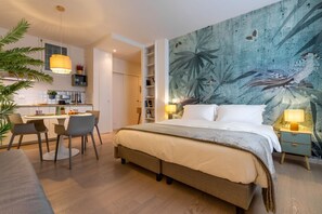 Moderni hotellihuone, jossa on sänky, yöpöydät, ruokailutila ja keittiö.