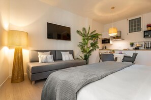 Moderni hotellihuone, jossa on sänky, sohva, työpöytä ja pieni keittiönurkkaus.
