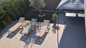 Un patio al aire libre con sillones de descanso y una mesa, rodeado de vegetación y un árbol.