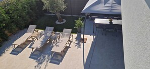 Eine Terrassensitzgruppe mit Lounge-Möbeln und Tisch, umgeben von Pflanzen und einem Baum.