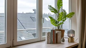 A room with a wooden desk, a potted plant, books, and a lamp. - Juan | Trendy Renovated Apartment in the Heart of Ostend | Sleeps 8 (Oostende)