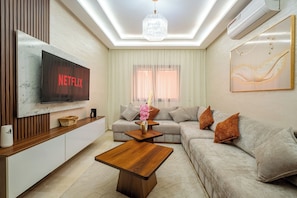 Ein modernes Wohnzimmer mit Flachbildfernseher, Couch, Holztisch und einer Kronleuchter.