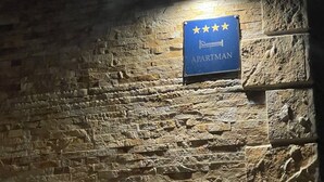 Un muro de piedra con un letrero que dice 'VILLA DETI 242' y un letrero azul con estrellas y la palabra 'APARTMAN'.