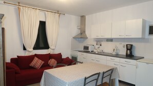 Una cocina compacta con armarios blancos, microondas, cafetera y mesa de comedor con sillas.