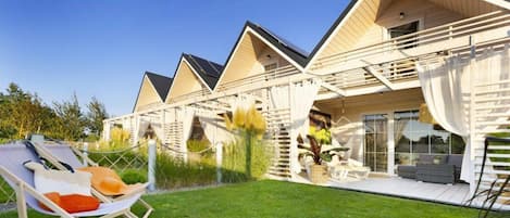 A row of modern, chalet-style buildings with large windows and balconies, a grassy lawn, and outdoor seating areas.