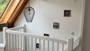 Una escalera con barandilla blanca, piso de madera y techo con tragaluz y lámpara colgante.