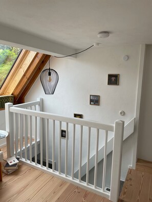 Eine Treppe mit weißer Handlauf, einem Holzboden und einer Decke mit Oberlicht und Pendelleuchte.
