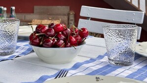 Una mesa con un bol de cerezas, dos vasos y un plato blanco.
