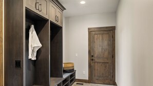 A hallway with a dark wooden bench, a white towel hanging, and a wooden door. - Whisper Ridge - Luxury 5 BD - Walk to Social Village (CLE ELUM)
