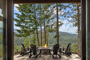 An outdoor seating area with a fire pit, surrounded by tall trees and a mountain view. - Whisper Ridge - Luxury 5 BD - Walk to Social Village (CLE ELUM)