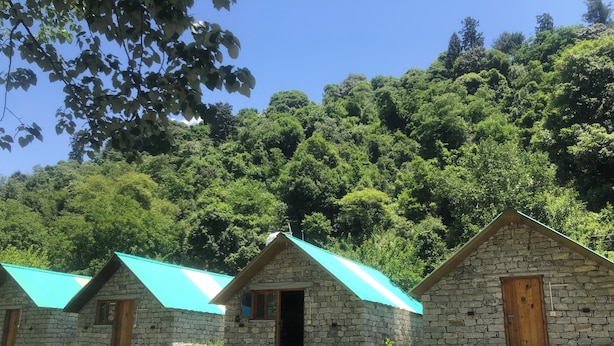Una hilera de cabañas de piedra con techos turquesa, frente a un denso bosque.