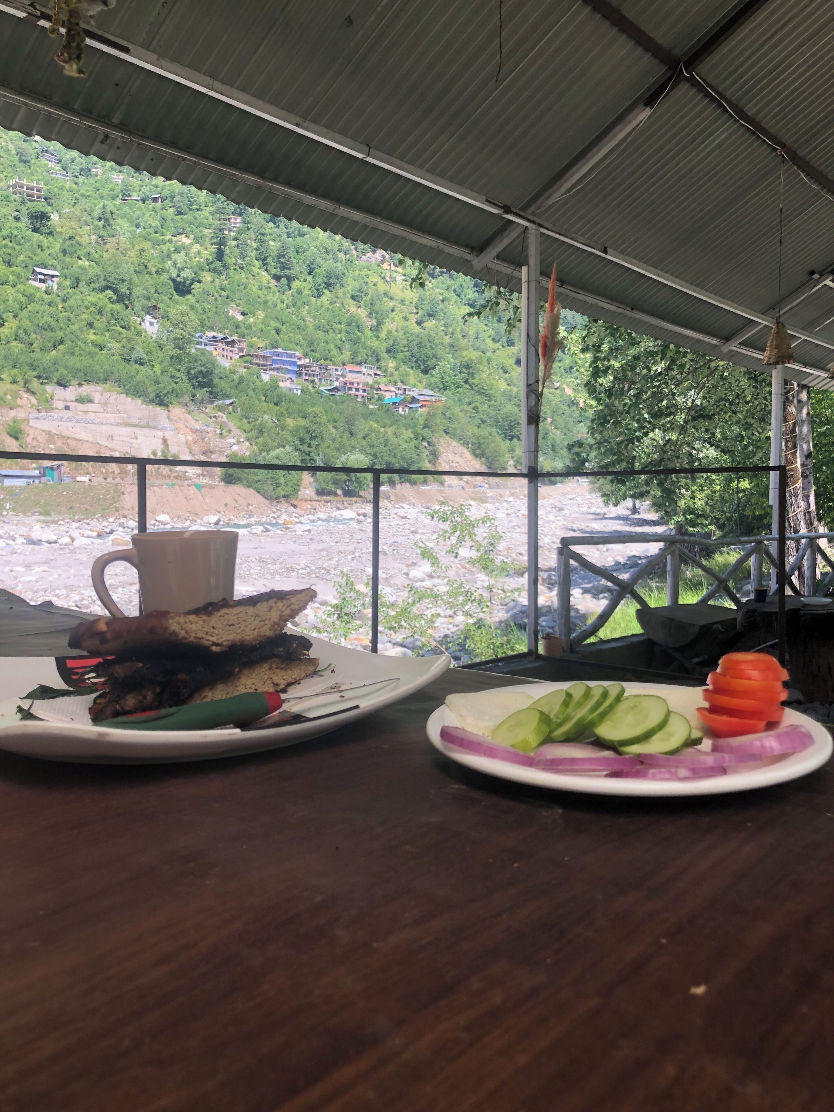 A table with a meal and a view of a river and greenery.