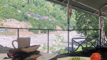 A table with a meal and a view of a river and greenery.