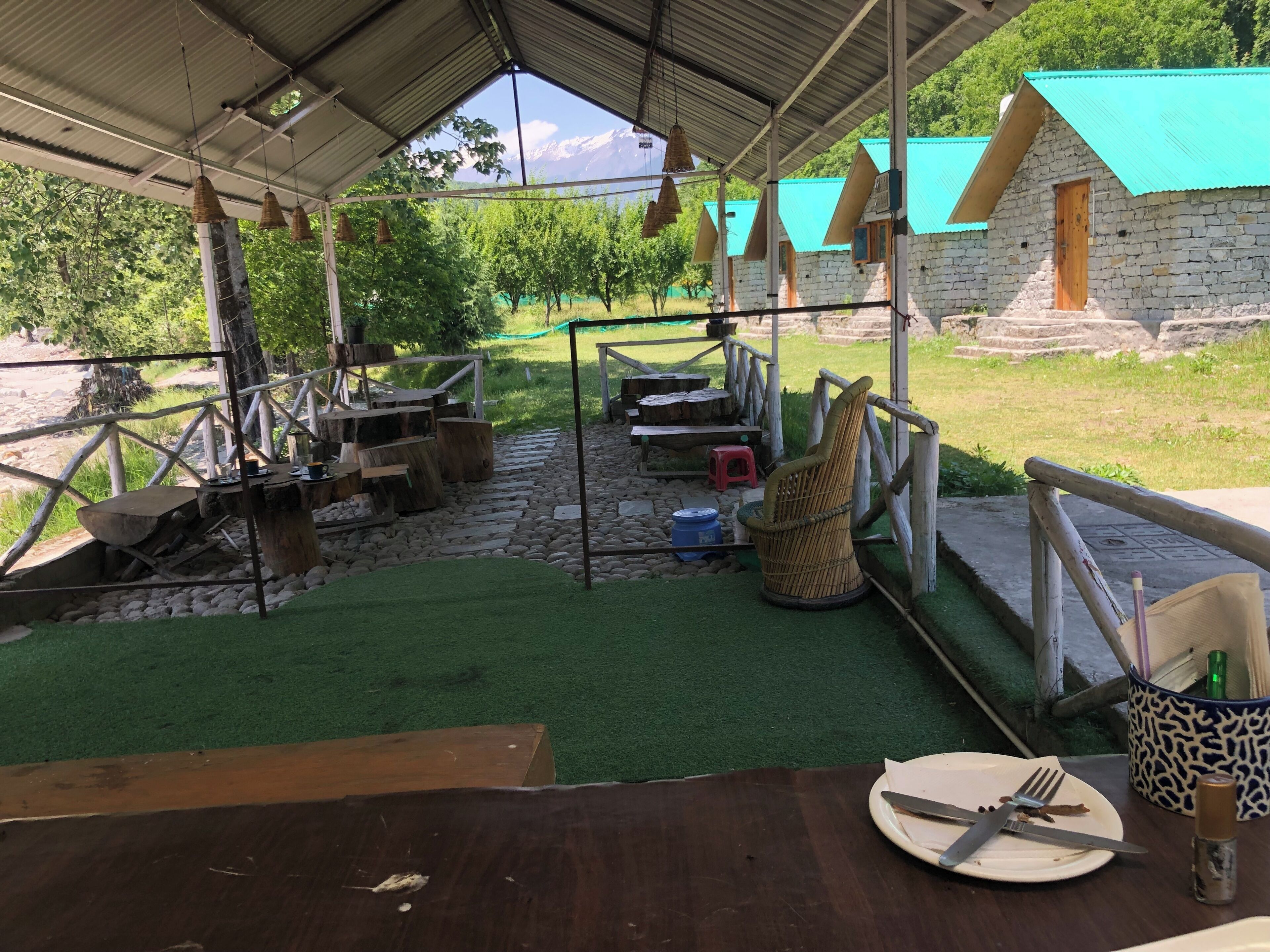 A rustic outdoor dining area with stone walls, a covered roof, and a view of mountains.