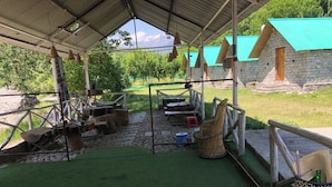 Un área de comedor al aire libre de estilo rústico, con muros de piedra, techo cubierto y vistas a montañas.