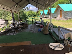 Un espace de restauration extérieur rustique, avec des murs en pierre, un toit abrité et une vue sur des arbres verdoyants et des montagnes.