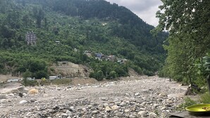 Un lecho de río pedregoso con casas en una ladera al fondo.