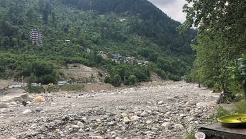 A rocky riverbed with houses on a hillside in the background.