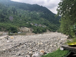 Un lit de rivière rocheux, parsemé de pierres, avec quelques bâtiments visibles au loin.