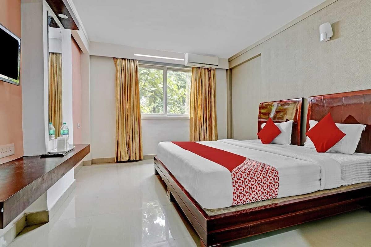Habitación de hotel con cama, televisión, escritorio y ventana con cortinas.