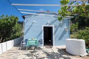 A small building with a blue exterior, a stone floor, a table with chairs, and a white cylindrical object.