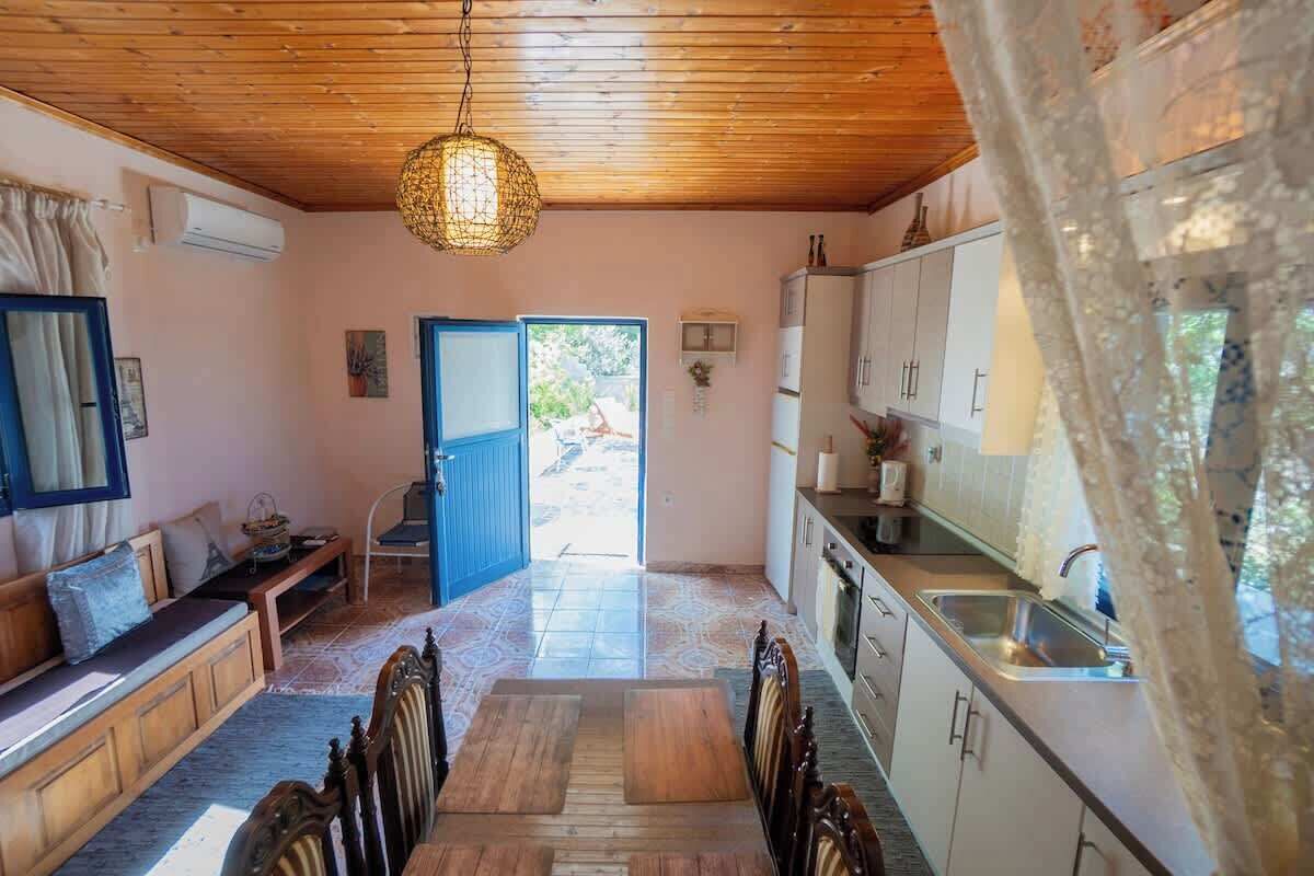 Ein Zimmer mit Holzboden, einem Esstisch mit Stühlen, einer Küchenzeile mit Schränken und einer Tür, die nach draußen führt.